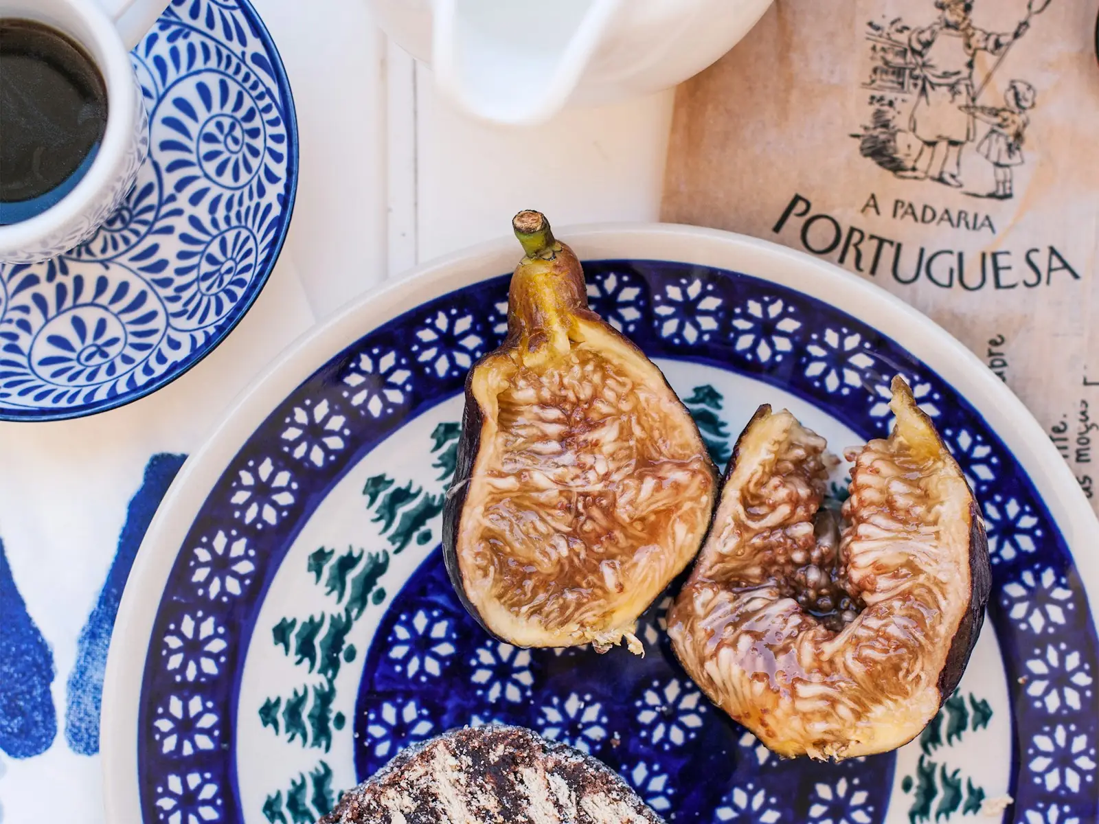 A cafe table with coffee, figs and chocolate salami served on blue and white Portuguese plates