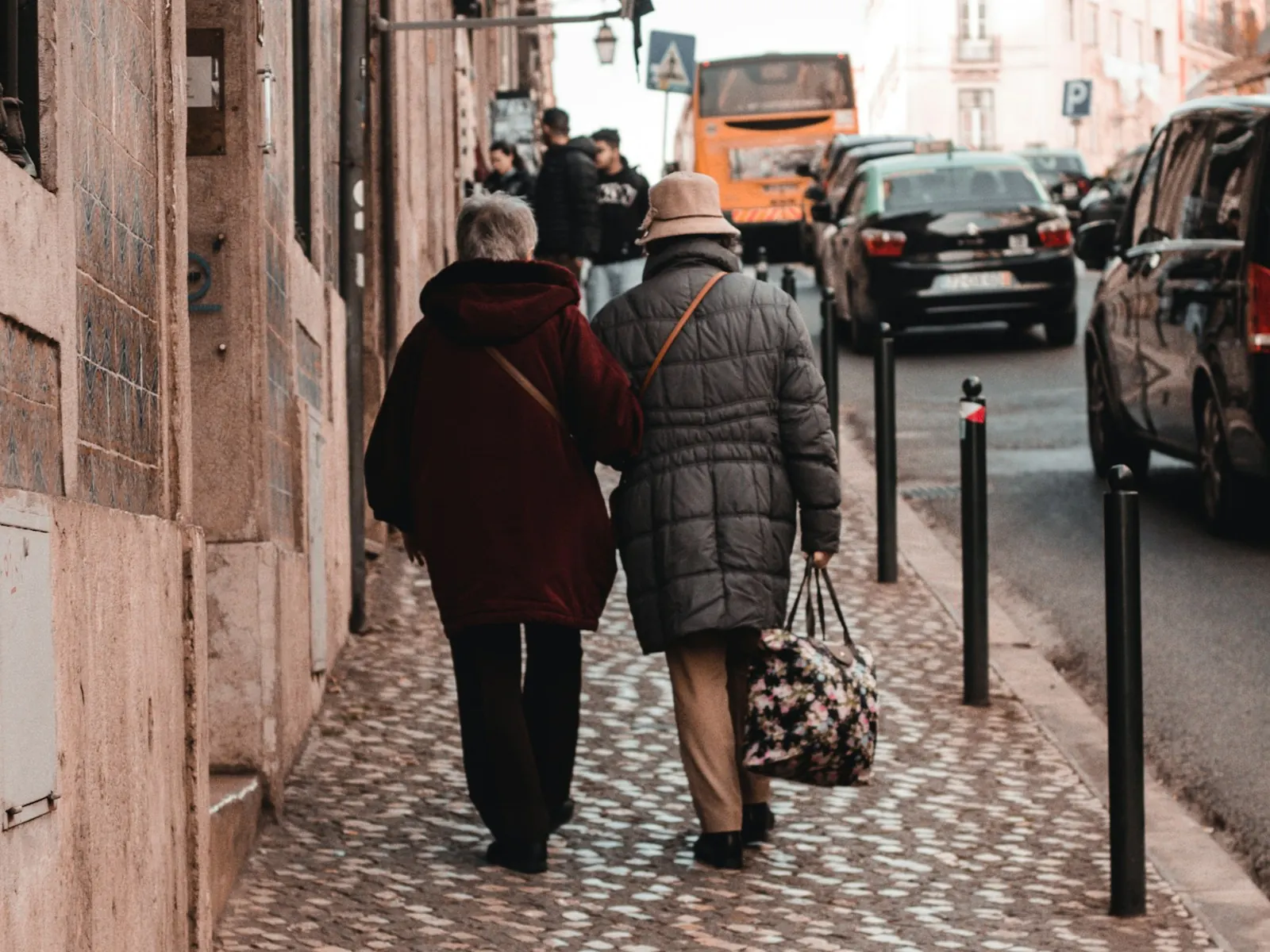 An older couple walking side by side, seen from behind, along a cobbled pavement in Lisbon